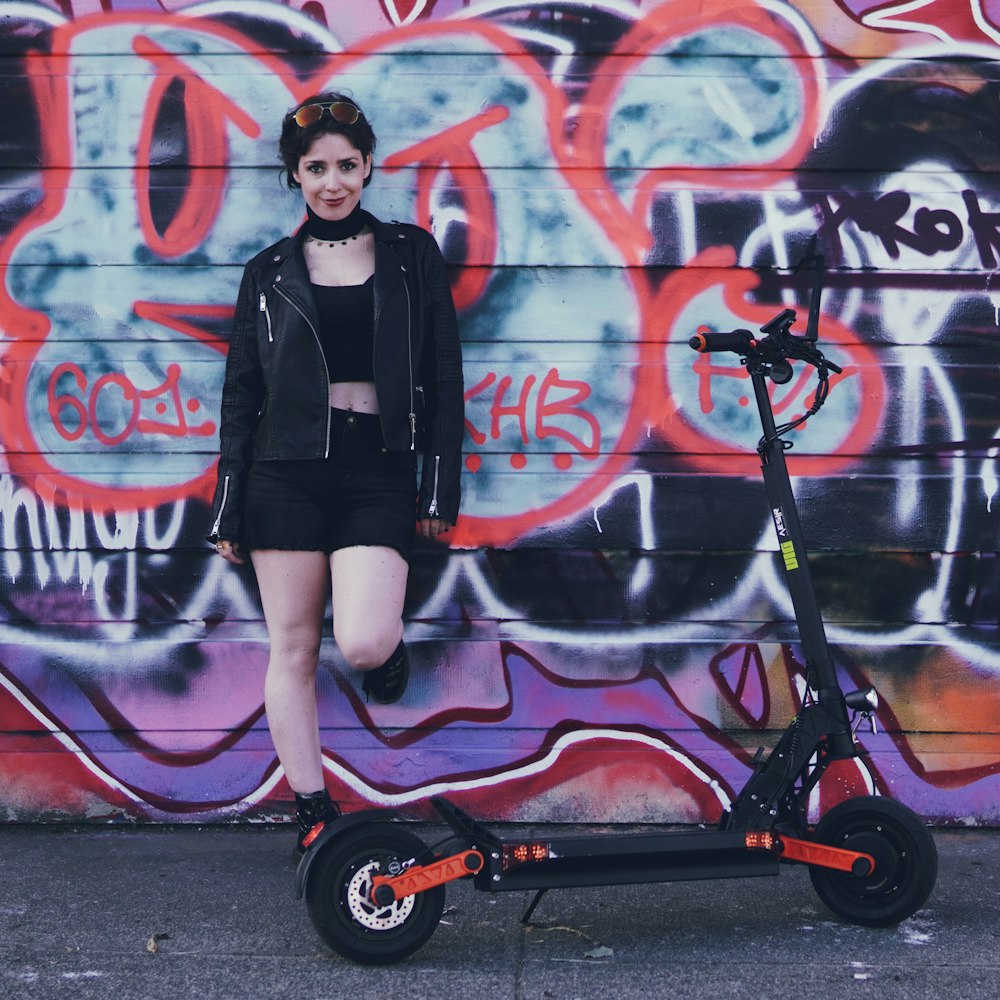 a woman standing next to a scooter in front of a wall with graffiti