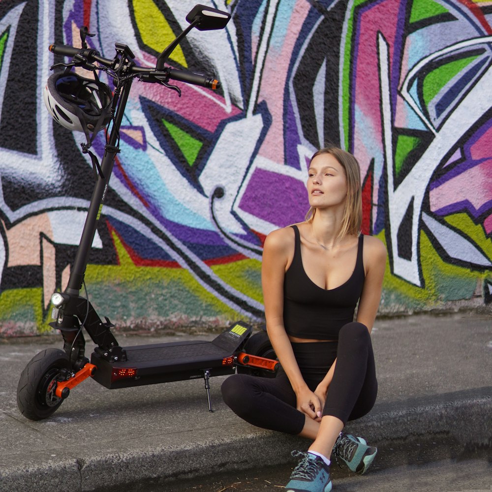 a woman sitting on the ground next to a scooter