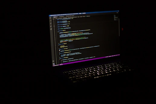 A developer writing code on a laptop with colorful lines of code glowing on the screen.