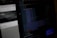 A computer screen displaying a dark-themed text editor with code in various colors. The left side shows the interface of a web inspector or development tool, with some unreadable elements beside the code. The background appears blurred with faint details of another screen or window.