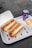 Two sandwiches filled with meat, cheese, and vegetables are placed in open cardboard boxes on a white tray. Next to them, there is a bowl containing fries topped with cheese sauce and a can of Pepsi.