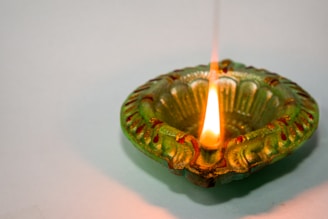 A decorative, green earthen lamp with intricate patterns is lit, casting a warm glow. The flame is vibrant and the lamp has red accents, highlighting its traditional design.