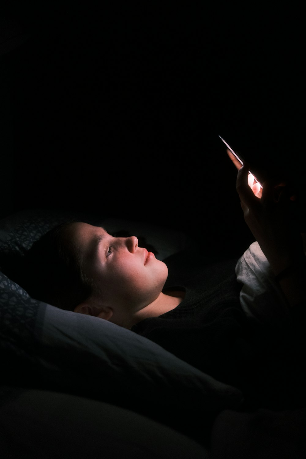 a woman laying in bed with a light on her face