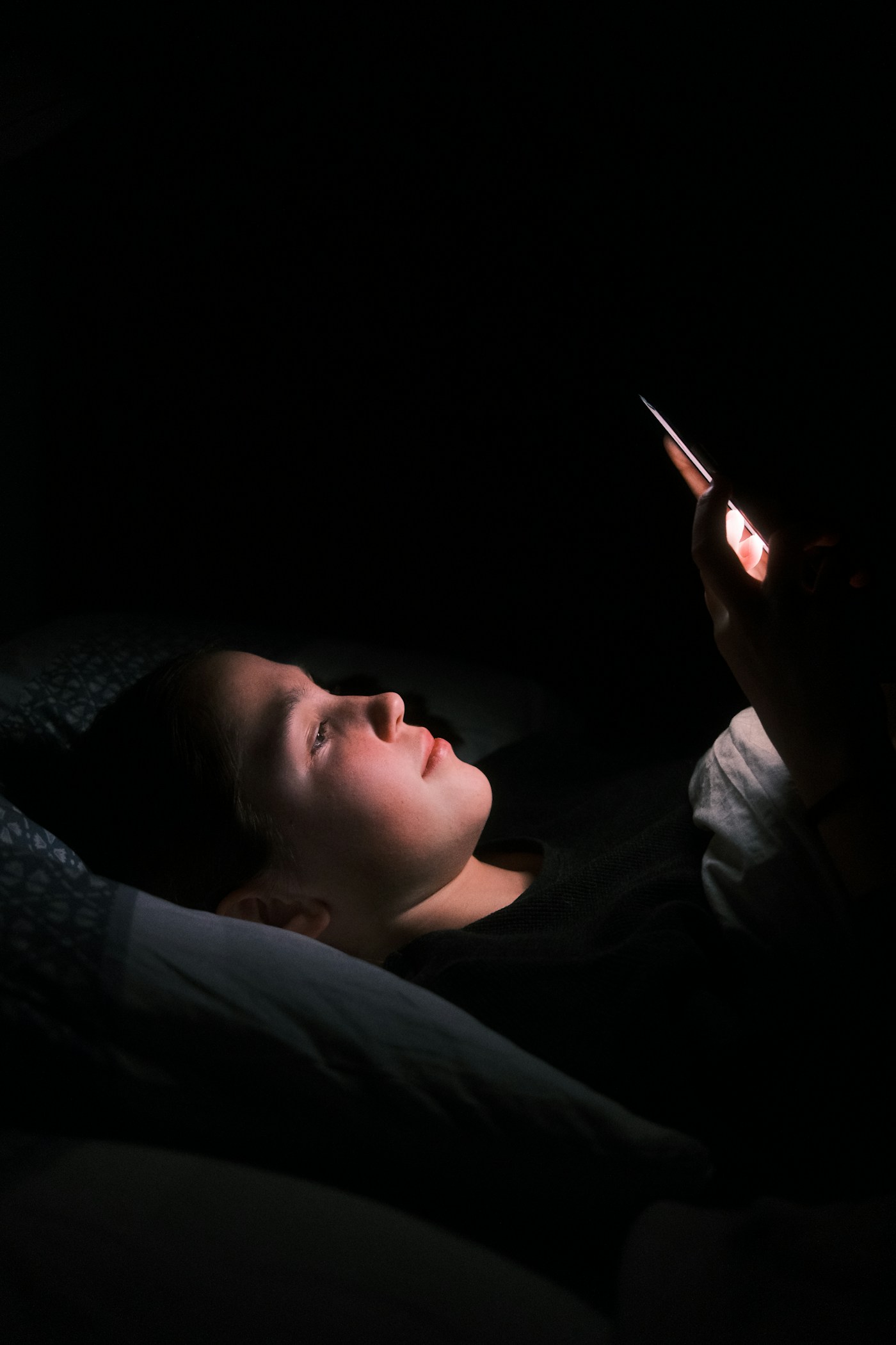 Mujer tumbada en la cama con la luz del móvil en la cara
