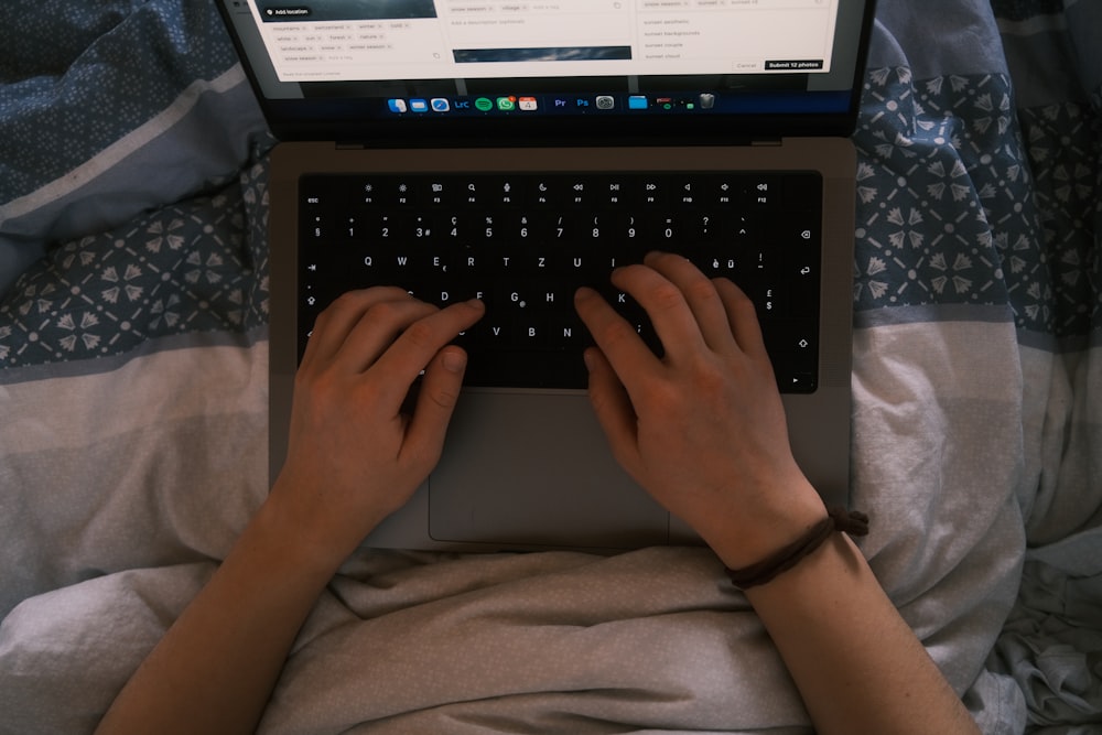 a person typing on a laptop on a bed