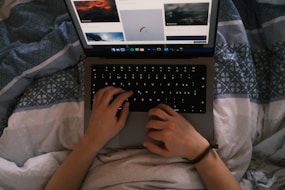 a person typing on a laptop on a bed