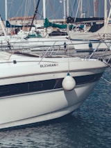 A white boat is docked at a marina, with many other boats visible in the background. The boat has a fender hanging on the side and identifiable registration DL2346AN. There are numerous masts and sails in the surrounding area.