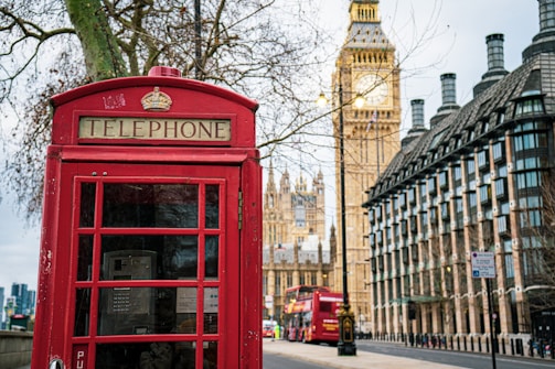 A cozy London street scene with classic red phone booths and a glimpse of the Thames River in the background.