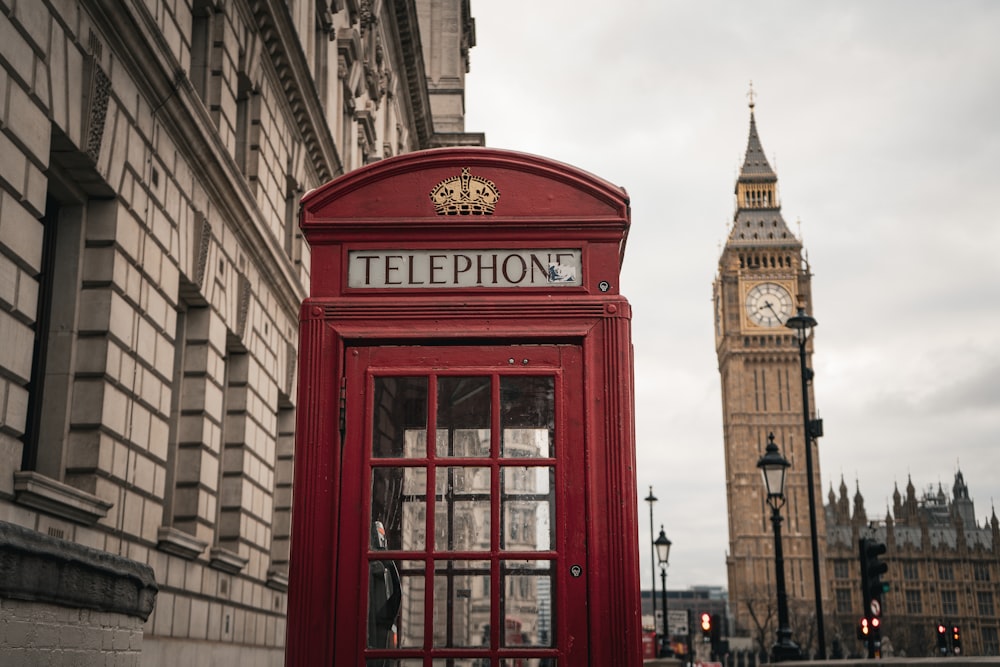 Una cabina telefónica roja frente a una torre del reloj