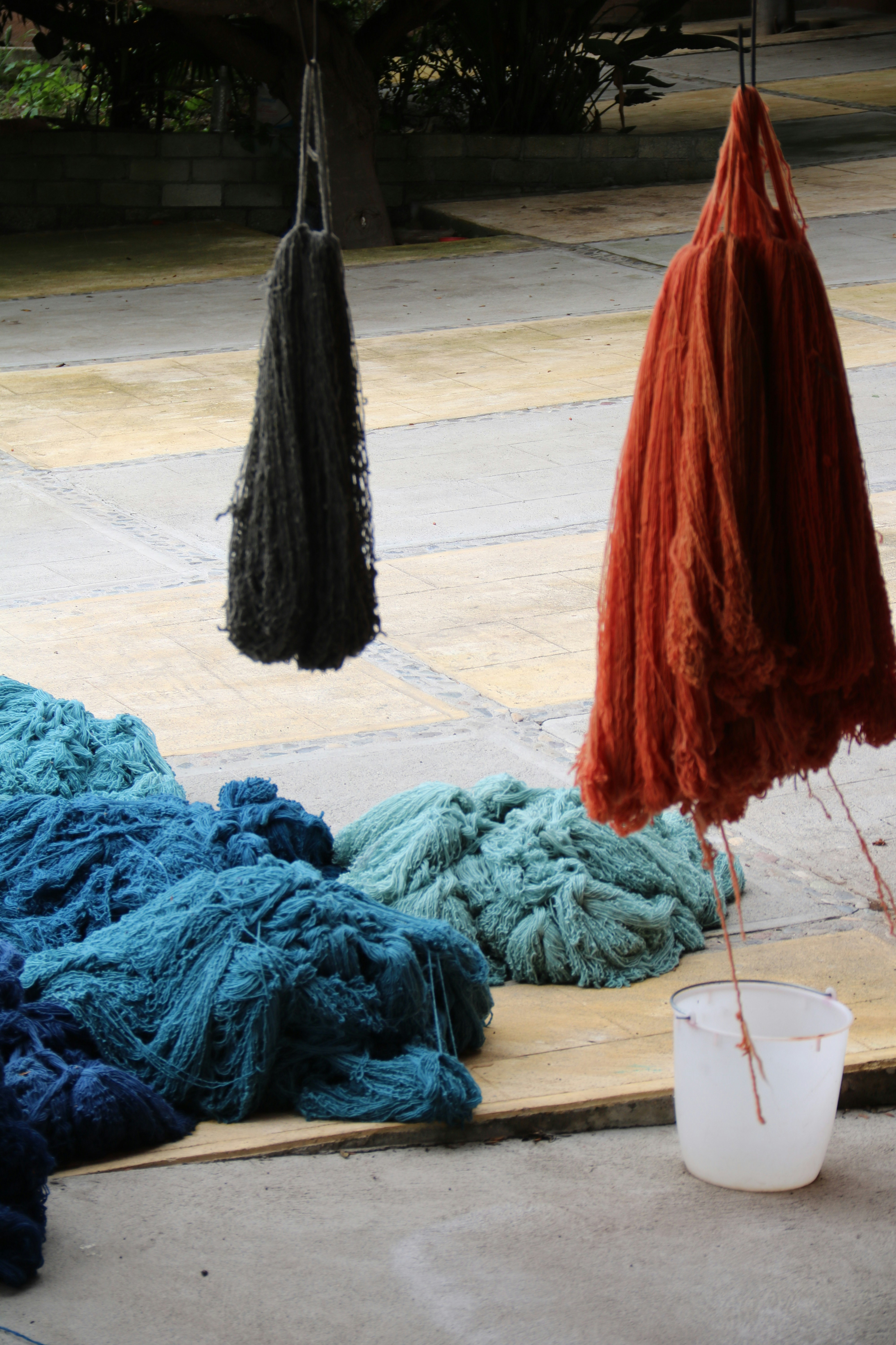 Vibrant dyed wool skeins hanging to dry in rich crimson, saffron, and indigo colors against white wall