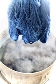 Artisan gently stirring a vat of deep indigo dye in natural light.