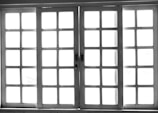A set of white-framed sliding glass doors with multiple square panes, allowing bright light to pass through, creating a high contrast between the dark frame and the bright background.