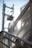 A close-up view of metallic railings and glass panels with sunlight creating reflections. A blurred background shows the outlines of an electrical pole and cables against a clear blue sky.
