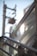 A close-up view of metallic railings and glass panels with sunlight creating reflections. A blurred background shows the outlines of an electrical pole and cables against a clear blue sky.