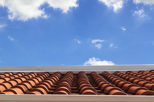 A roof with terracotta tiles under a bright blue sky featuring scattered white clouds.
