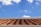 A roof with terracotta tiles under a bright blue sky featuring scattered white clouds.