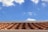 A roof with terracotta tiles under a bright blue sky featuring scattered white clouds.