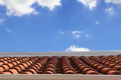 A roof with terracotta tiles under a bright blue sky featuring scattered white clouds.