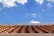 A roof with terracotta tiles under a bright blue sky featuring scattered white clouds.