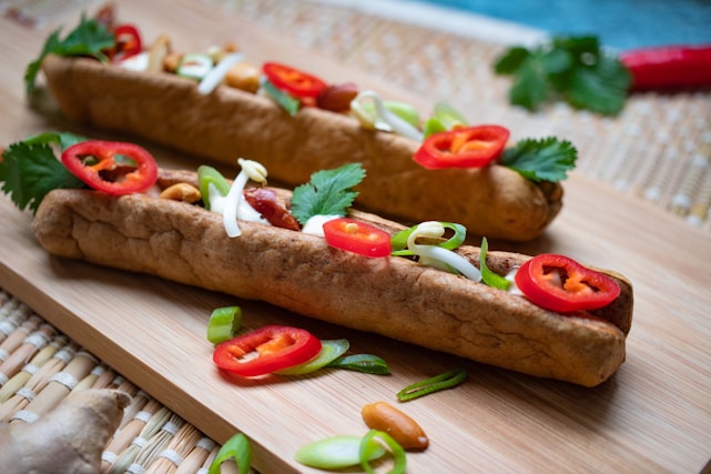 two hot dogs with toppings on a cutting board