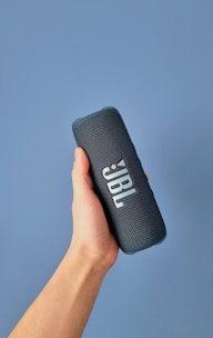 a hand holding a bluetooth speaker against a blue background