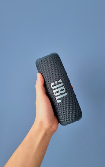 a hand holding a bluetooth speaker against a blue background