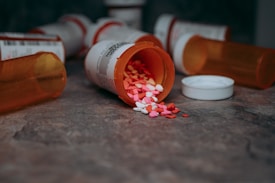 Several prescription pill bottles are scattered on a surface, some lying on their sides with colorful heart-shaped pills spilling out.