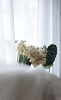 A serene morning light filtering through creamy curtains over a softly arranged bouquet of wildflowers on a wooden table.