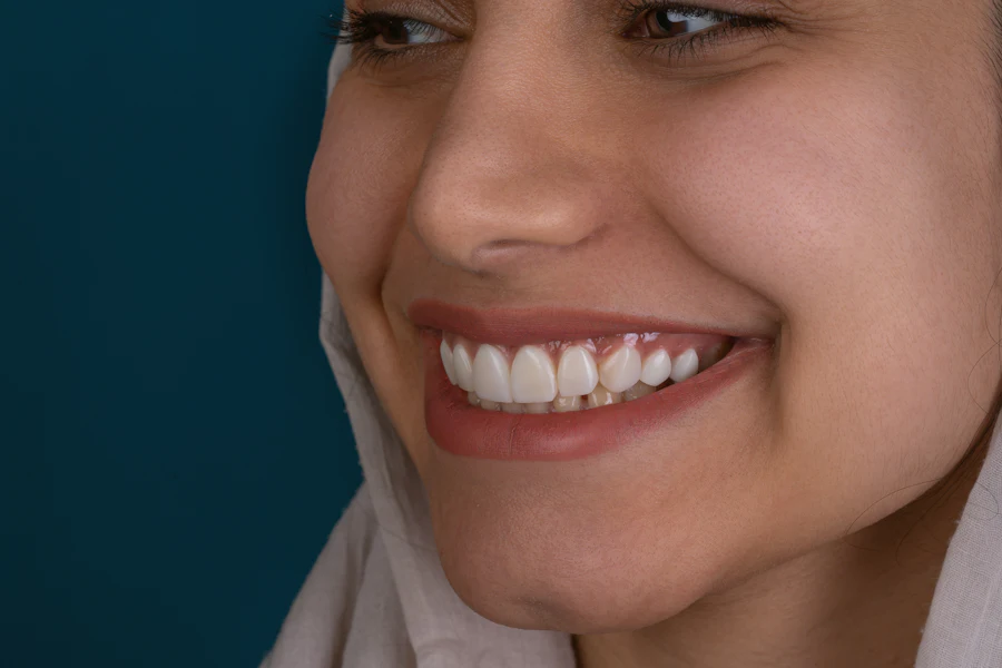 Close-up of a patient smiling to one side against a deep teal backdrop, showing healthy, natural-looking front teeth.