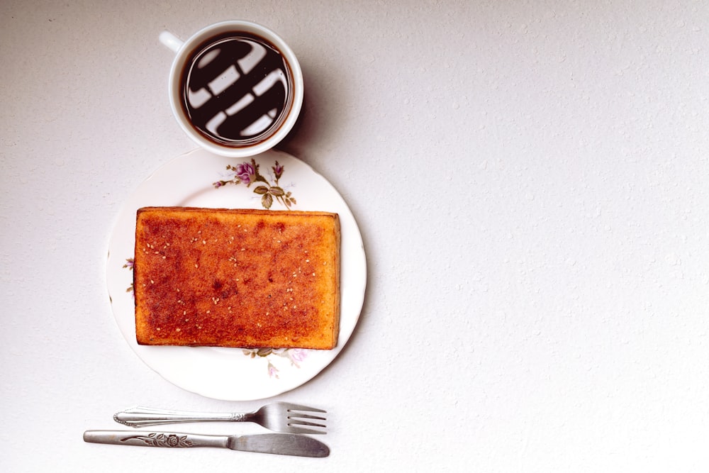 a piece of cake on a plate next to a cup of coffee