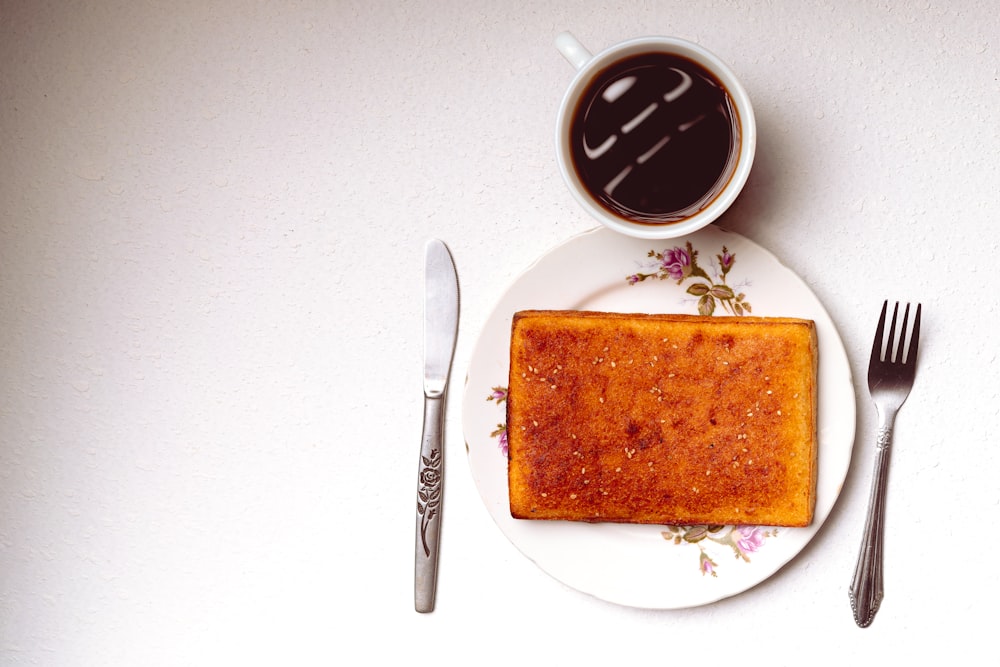 a white plate topped with a piece of cake next to a cup of coffee