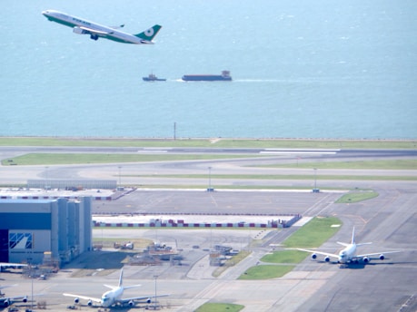 An airplane taking off with cargo containers being loaded in the background at an airport.