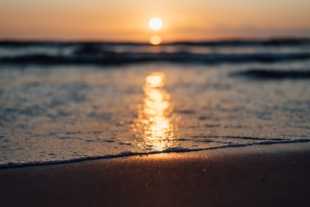 the sun is setting over the water at the beach