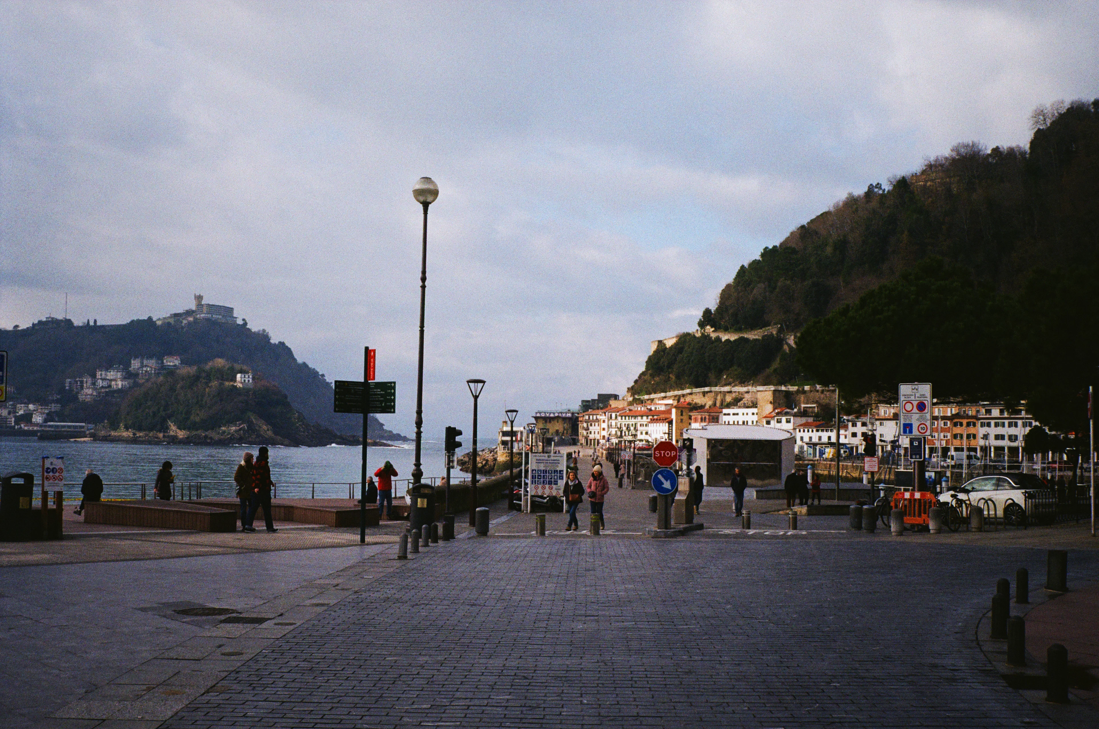 Strollers on the promenade beside La Concha bay in San Sebastian, with the green slopes of Monte Igueldo rising across the water