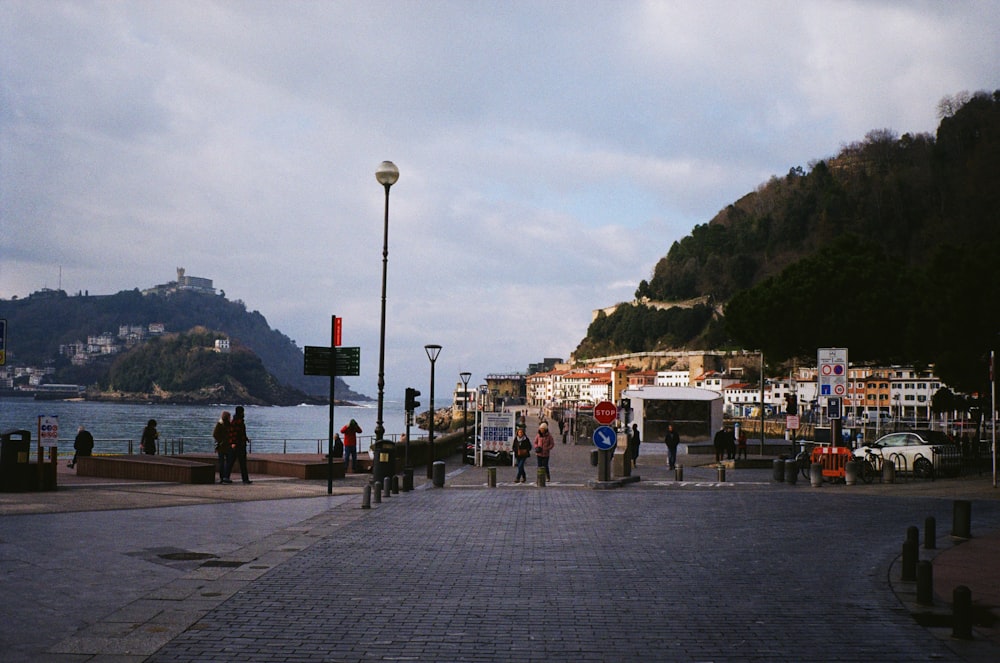 a group of people walking down a street next to a body of water