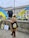 A person stands holding a large Ukrainian flag in front of a historic building. Nearby, other flags and placards are leaning against a wall. A black statue commemorating women of World War II is visible. In the background, police vehicles and an unseen monument can also be seen.