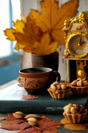 A joyful scene of a hand holding a bright red ceramic cup filled with tea, surrounded by scattered autumn leaves.