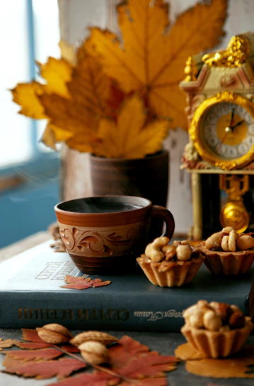 A cozy scene featuring a colorful stoneware cup filled with steaming tea, surrounded by autumn leaves.