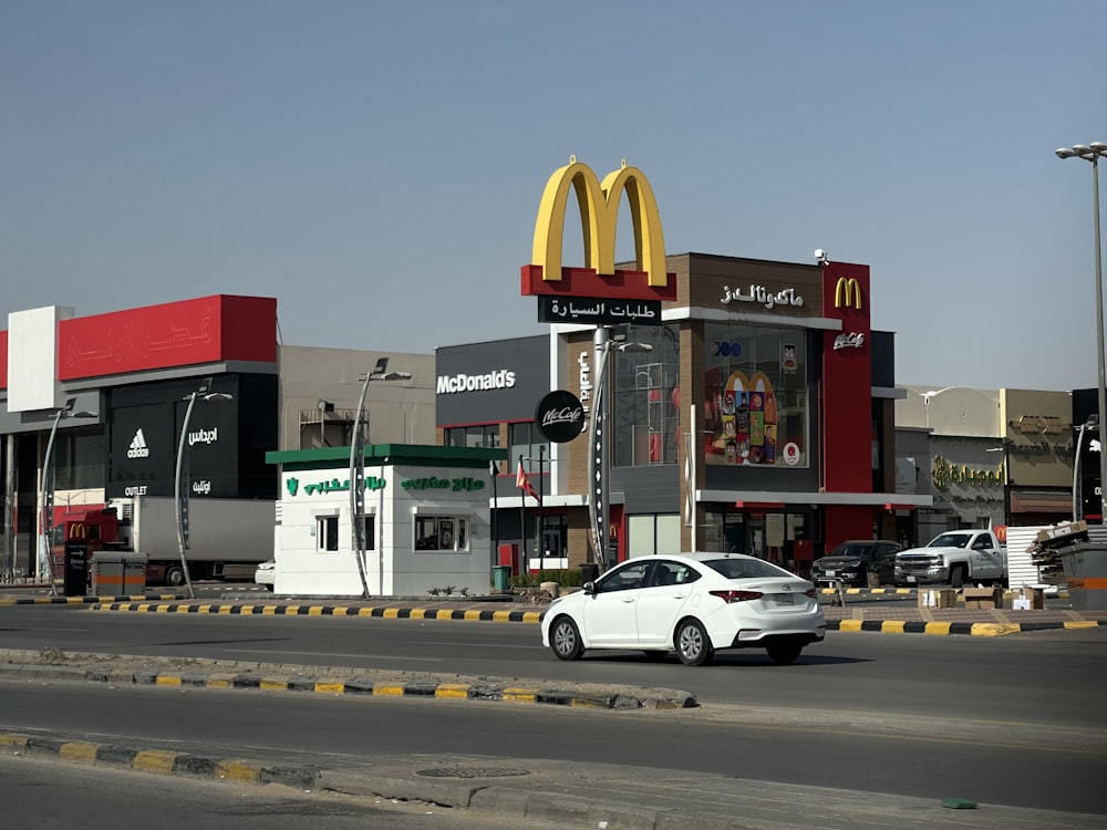 Ein weißes Auto fährt eine Straße neben einem McDonald's entlang