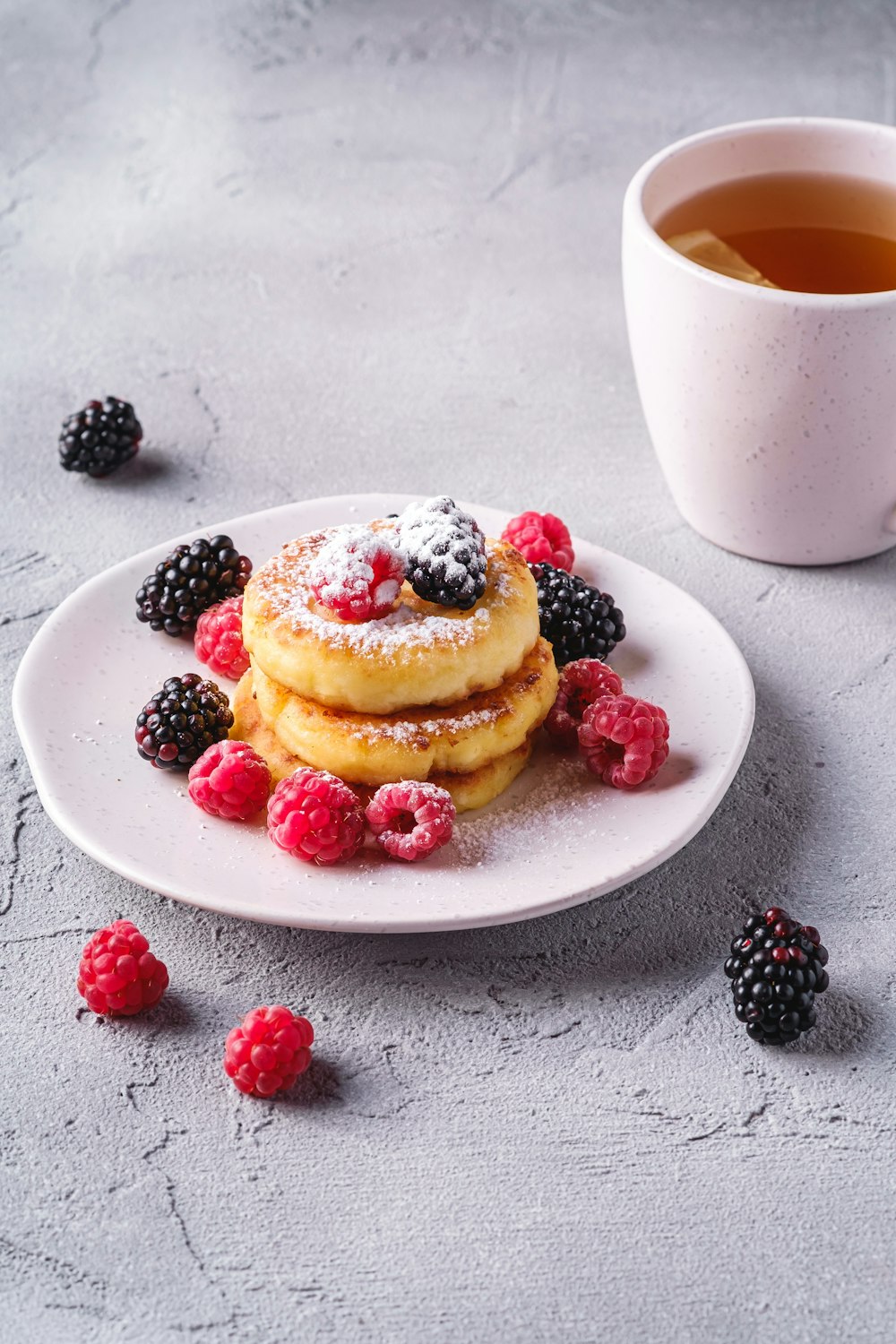 un piatto di frittelle con frutti di bosco e una tazza di tè