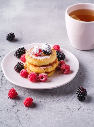 a plate of pancakes with berries and a cup of tea