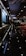 A dimly lit corridor in a modern establishment with reflective marble flooring, overhead lights, tables with red chairs on one side, and a sign reading 'Chaat Bazaar' on the other. The ceiling features intricate design with recessed lighting. The atmosphere appears elegant and contemporary.