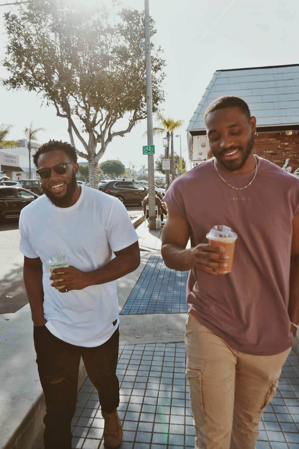 two men walking down a sidewalk holding drinks