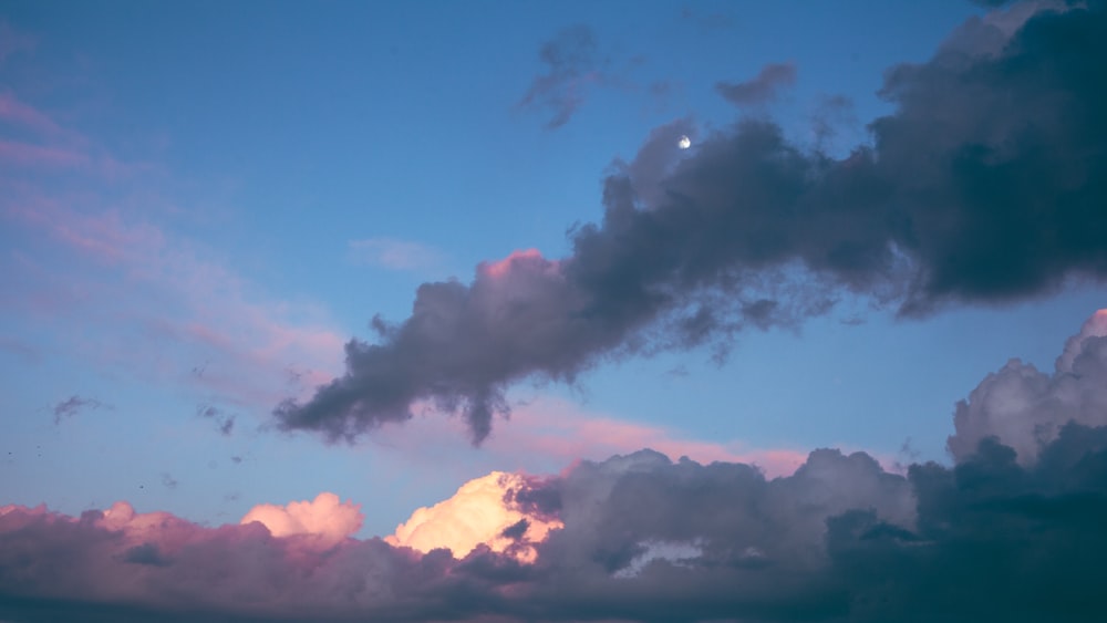 a cloud filled sky with a half moon in the distance