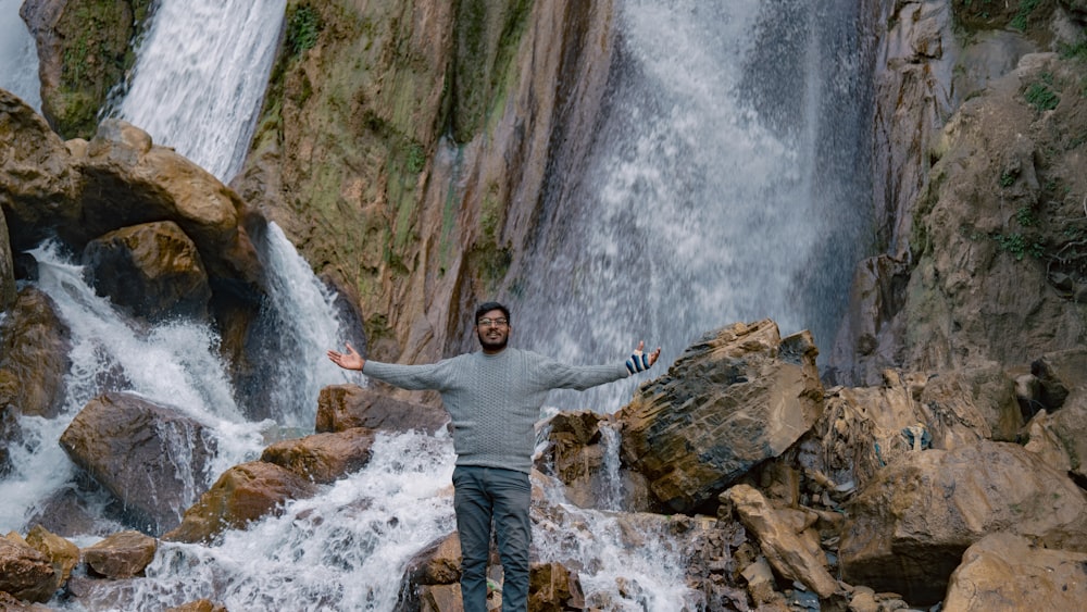 a man standing on rocks in front of a waterfall