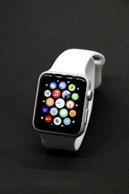 A sleek smartwatch with a silver case and a white band, featuring a vibrant display showing various app icons against a dark background.