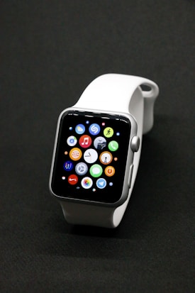 A sleek smartwatch with a silver case and a white band, featuring a vibrant display showing various app icons against a dark background.