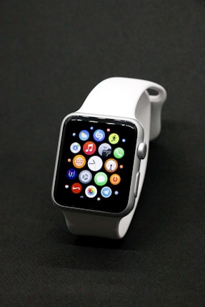 A sleek smartwatch with a silver case and a white band, featuring a vibrant display showing various app icons against a dark background.