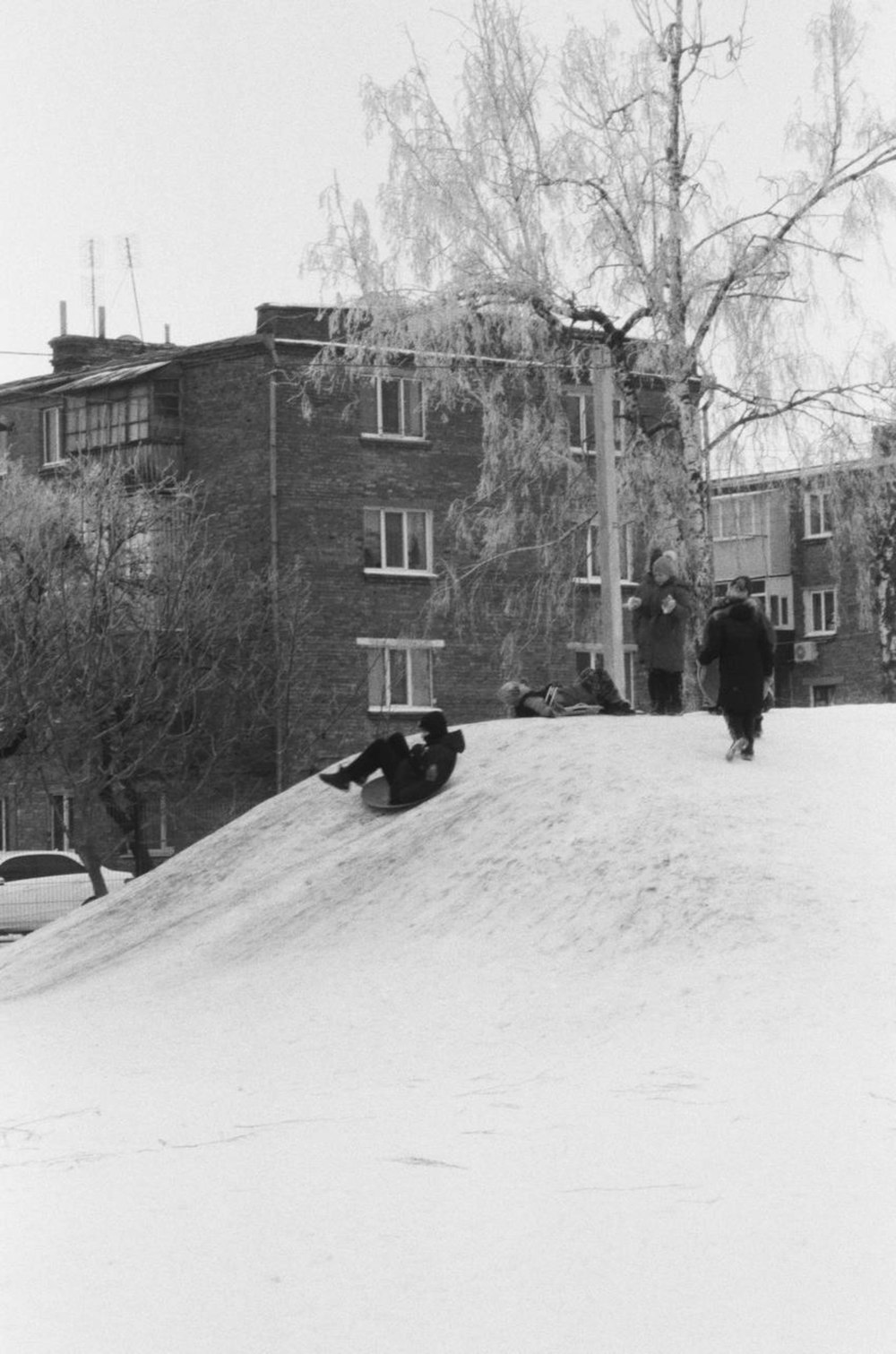 two people walking up a snowy hill in front of a building