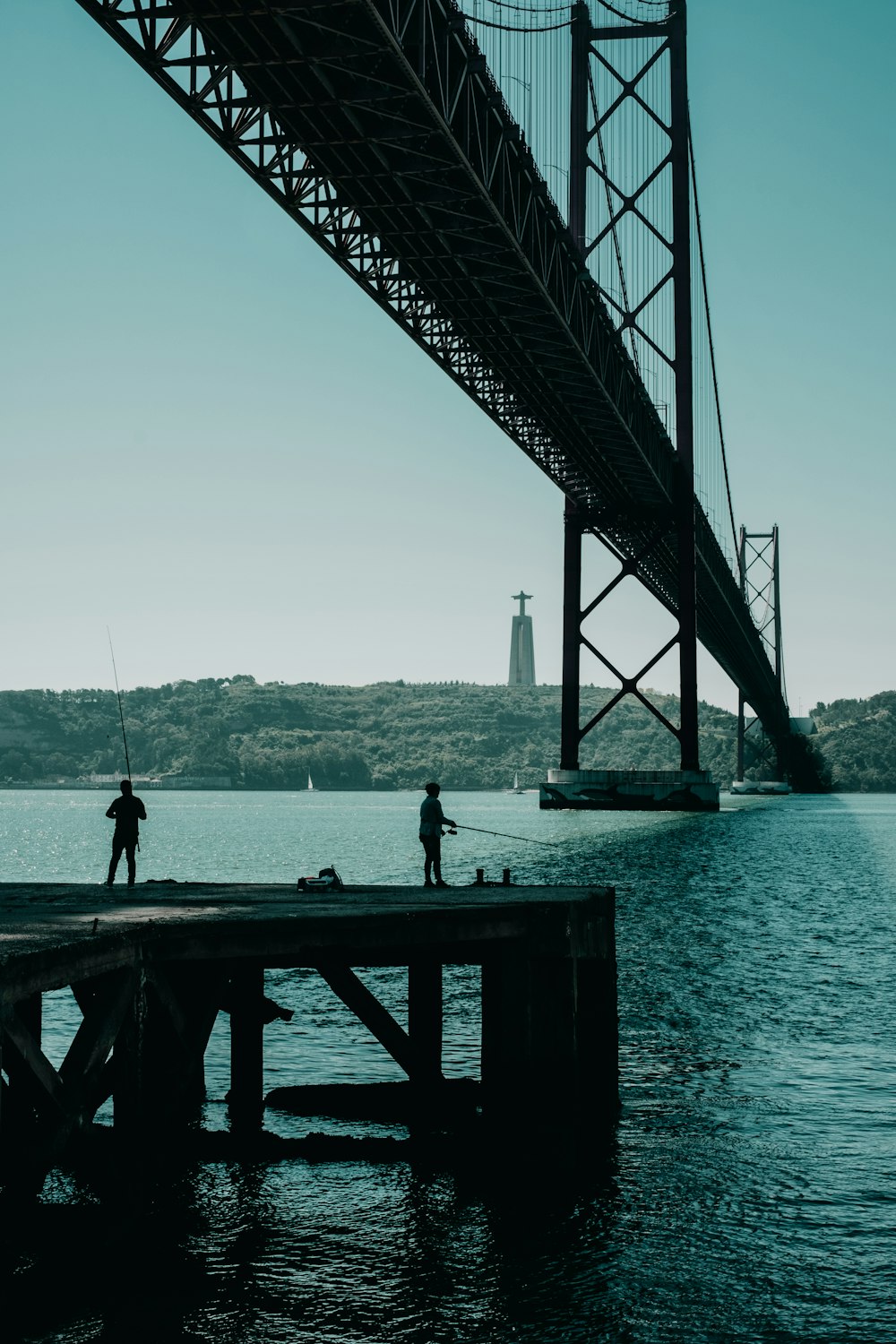 two people fishing from a pier under a bridge